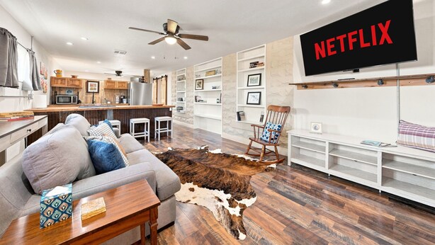 A modern living room with a sofa, a television mounted on the wall, and a cowhide rug. - Buttons on the Pedernales Casita - Riverview (Stonewall)