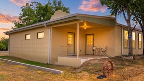 A single-story building with a covered porch, a small outdoor seating area, and a visible address sign. - Buttons on the Pedernales Casita - Riverview (Stonewall)