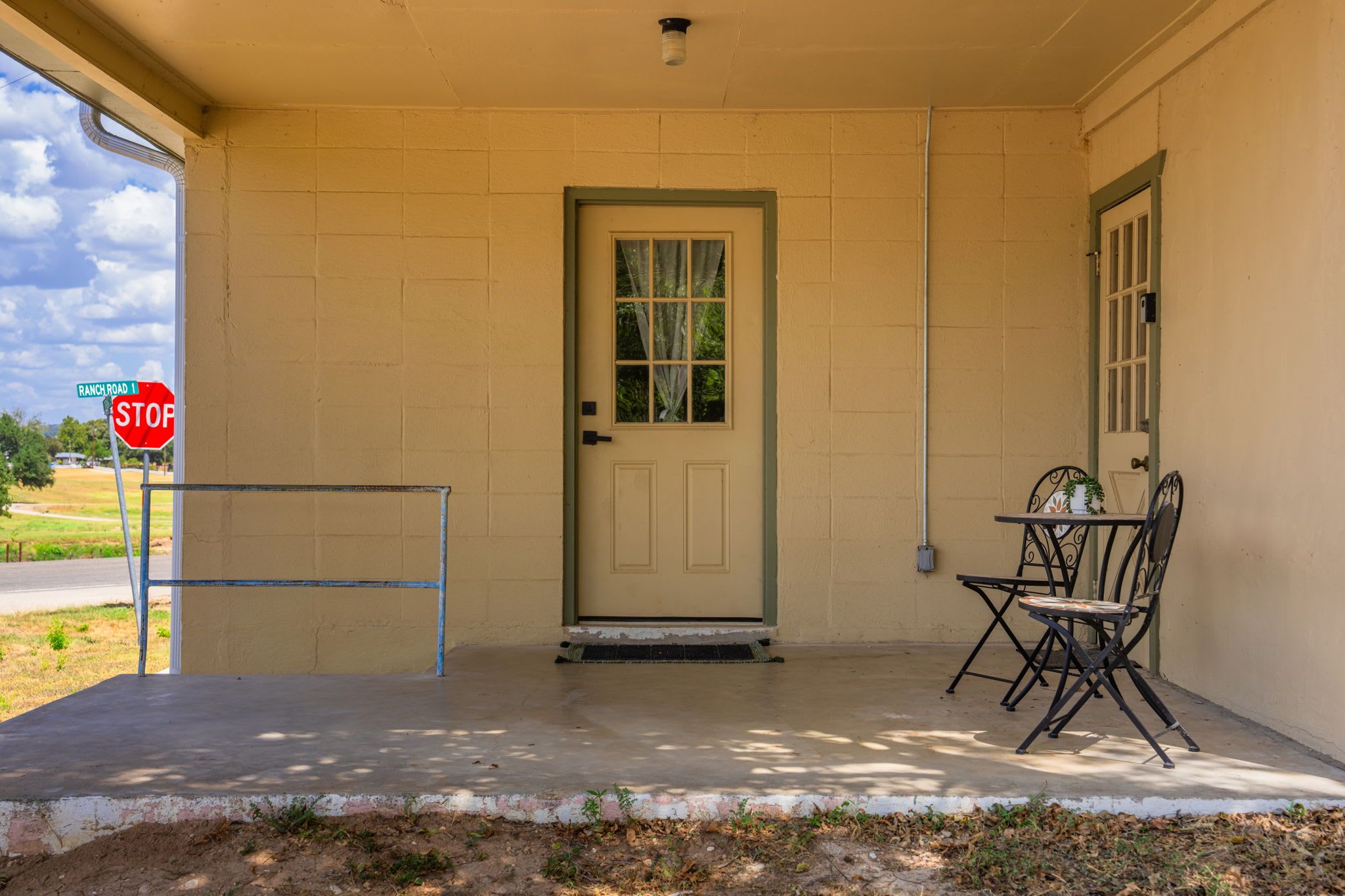 A building entrance with a beige door, a stop sign, and a metal chair outside.