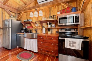 A compact kitchen with wooden walls, a stainless steel refrigerator, a microwave, and an oven. - Saw Mill (Lodge #4) Hot Tub & 10 Mins to Main St (Fredericksburg)