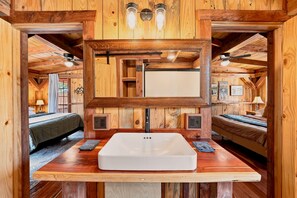 A wooden interior with a central sink, two beds, and a large mirror. - Saw Mill (Lodge #4) Hot Tub & 10 Mins to Main St (Fredericksburg)