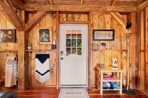 A wooden cabin interior with a white door, a welcome mat, a shelf with books, and a wall-mounted sign. - Saw Mill (Lodge #4) Hot Tub & 10 Mins to Main St (Fredericksburg)