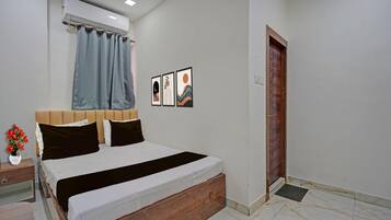 A bedroom with a bed, a nightstand, a potted plant, and a door.