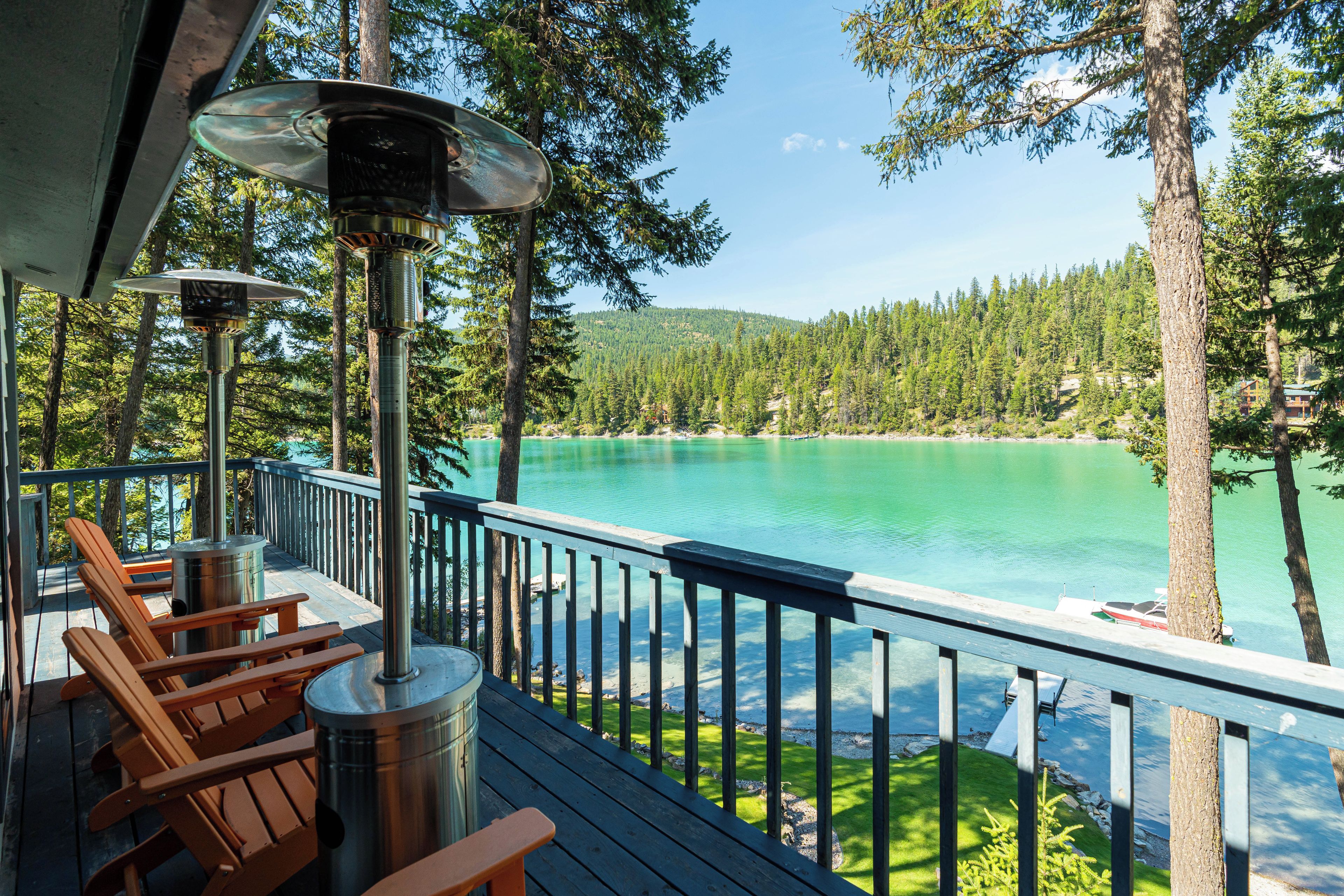 Une terrasse avec coin salon extérieur, un barbecue et une vue sur un lac entouré d’arbres.