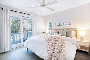 Ein Schlafzimmer mit einem großen Bett, einem Deckenventilator, Blick ins Freie durch eine Schiebetür und einem Nachttisch mit Lampe.