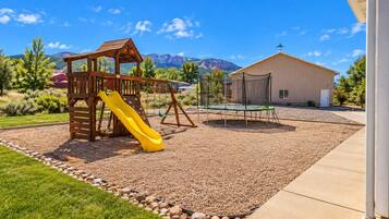 Un parque infantil con tobogán y columpios, rodeado de grava y un edificio al fondo.