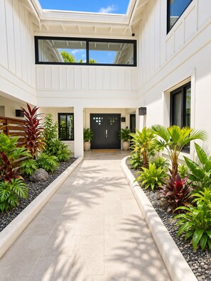A modern two-story building with a central entrance, surrounded by a variety of tropical plants and a tiled pathway. - Camp Bay Beach House – Private Pool and Beachfront (Camp Bay)