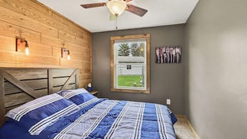 Une chambre à coucher avec un lit, un ventilateur de plafond, une fenêtre donnant sur un beau paysage et un luminaire fixé au mur.