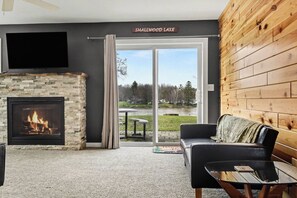 A living room with a fireplace, a sofa, a coffee table, and a view of a lake.