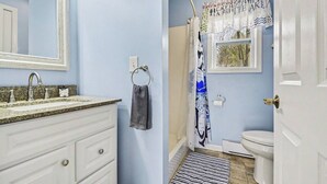 Ein Badezimmer mit Waschbecken, Spiegel, Handtuchhalter, Duschvorhang, Toilette und einer Tür.