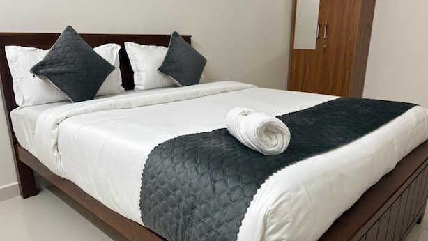 Een bed met een wit en donker gewatteerd sprei, twee kussens en een opgerolde witte handdoek.
