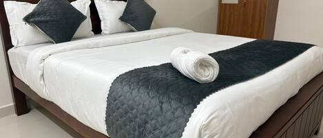 A bed with a white and dark quilted bedspread, two pillows, and a rolled white towel.