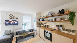 A modern kitchen with wooden countertops, a built-in oven, and a dining area with a bench and a TV. - Porthminster Pad | St Ives, Parking, 2 min walk to Porthminster Beach (Saint Ives)