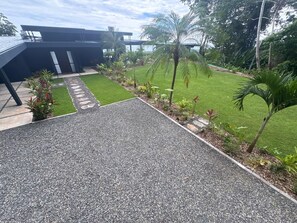 A modern building with a gravel driveway leading to a well-maintained lawn and palm trees. - NEW OASIS! Excellent panoramic views, private pool brand new. (Savegre)