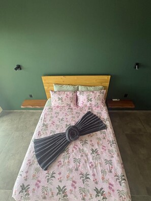Ein Bett mit einer blumigen Tagesdecke und einem dunkel gefärbten, fächerförmigen Kissen.