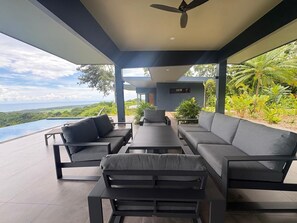 A modern outdoor seating area with a view of the ocean and lush greenery. - NEW OASIS! Excellent panoramic views, private pool brand new. (Savegre)
