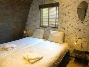 A bedroom with a bed, pillows, a window with blinds, a bedside lamp, and a mirror on the wall. - Group Stay Near Schoorl Dunes (Schoorl)