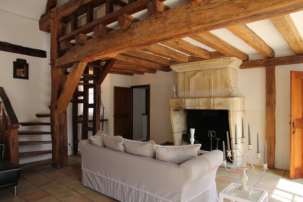 Una stanza con soffitto in legno, camino, divano e una scala.