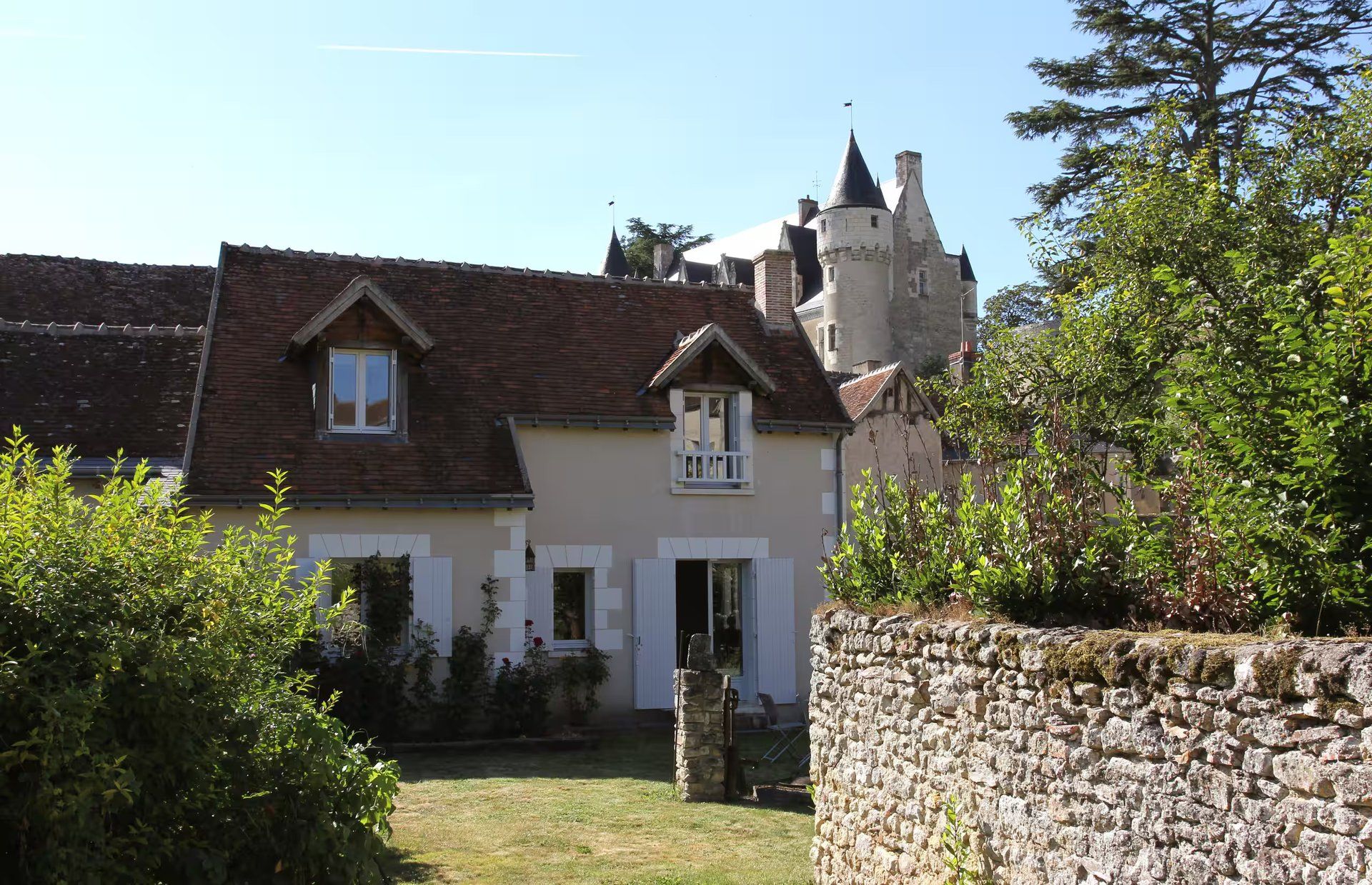 Un bâtiment traditionnel en pierre, doté d’un toit à deux versants, d’une petite construction adjacente avec un toit en pignon et d’un mur de pierre percé d’une porte.