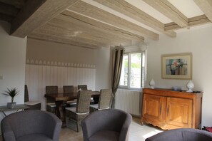 A room with a dining table, wicker chairs, a grey sofa, a wooden cabinet, and a painting on the wall. - Maison de Charme 6p - Montrésor (Montrésor)