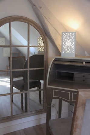 Ein Zimmer mit einem großen Bogenfenster, einem Schreibtisch mit Schubladen und einer dekorativen Leuchte.