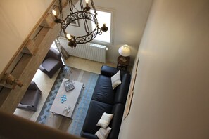 A high-ceilinged living room with a black sofa, a coffee table, and a patterned rug. - Maison de Charme 6p - Montrésor (Montrésor)