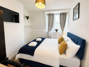 Ein Hotelzimmer mit Bett, Wandfernseher, Vorhängen an einem Fenster und einem Tisch mit Pflanze.