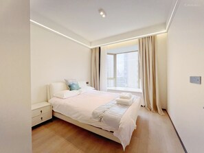 A modern bedroom with a large bed, bedside tables, and a window with curtains.