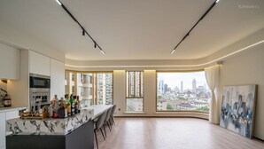 A modern kitchen with a marble countertop and bar area, large windows with a city view, and a painting on the wall.