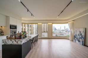 Cozinha moderna com bancada de mármore e área de bar, grandes janelas com vista para a cidade e um quadro na parede.