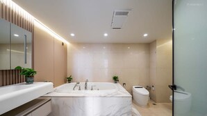 A modern bathroom with a large bathtub, a separate toilet, and a glass shower enclosure.