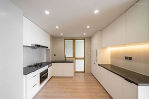 Cozinha moderna com armários brancos, bancada preta e iluminação embutida no teto.