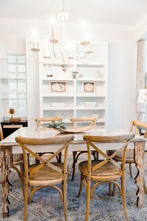 Ein Essbereich mit einem weißen Tisch, Holzstühlen und einer Chandelier.