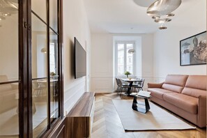 A modern living room with a sofa, a dining table with chairs, a TV mounted on the wall, and a large window. - Stylish 1BR 2Bath Apartment near Castel Sant'Angelo — Prati, Rome (Rome)