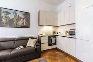 A compact kitchen with white cabinets, a black oven, and a dining area with a brown leather sofa. - Stylish 1BR 2Bath Apartment near Castel Sant'Angelo — Prati, Rome (Rome)