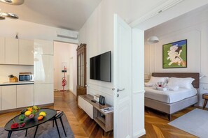 A modern hotel room with a bed, a TV, a kitchenette, and a dining area with fruit. - Stylish 1BR 2Bath Apartment near Castel Sant'Angelo — Prati, Rome (Rome)