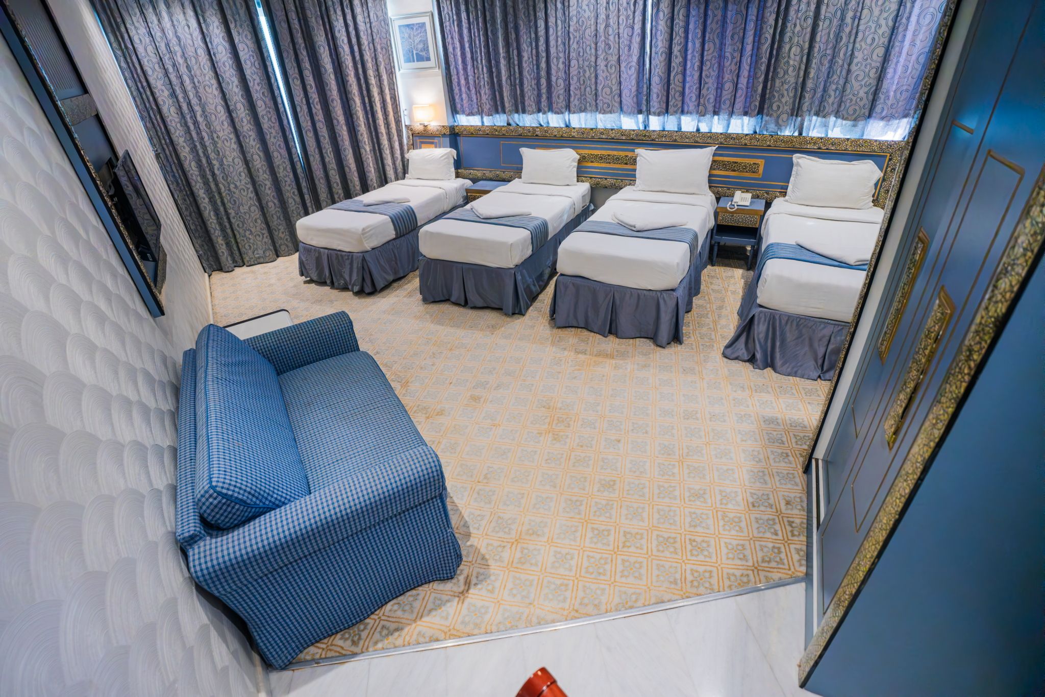 Una habitación de hotel con sofá, dos camas individuales, alfombra estampada y cortinas.
