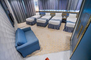 A hotel room with a sofa, two single beds, a patterned carpet, and curtains. - فندق تلال اليقين (Makkah)