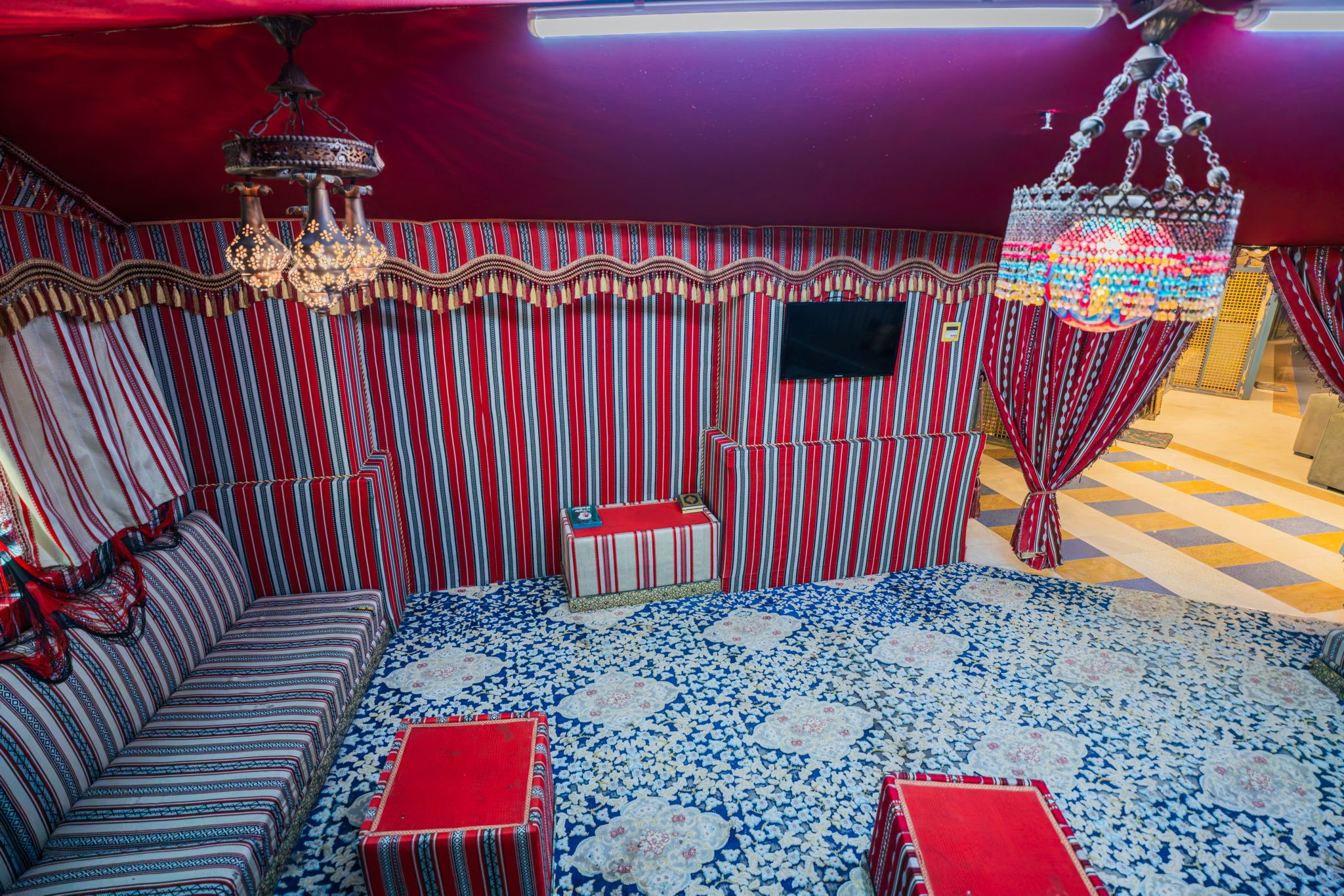 A room with striped walls, a sofa, a small table, a decorative chandelier, and a patterned carpet.