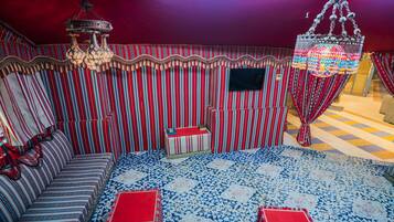 A room with striped walls, a sofa, a small table, a decorative chandelier, and a patterned carpet.