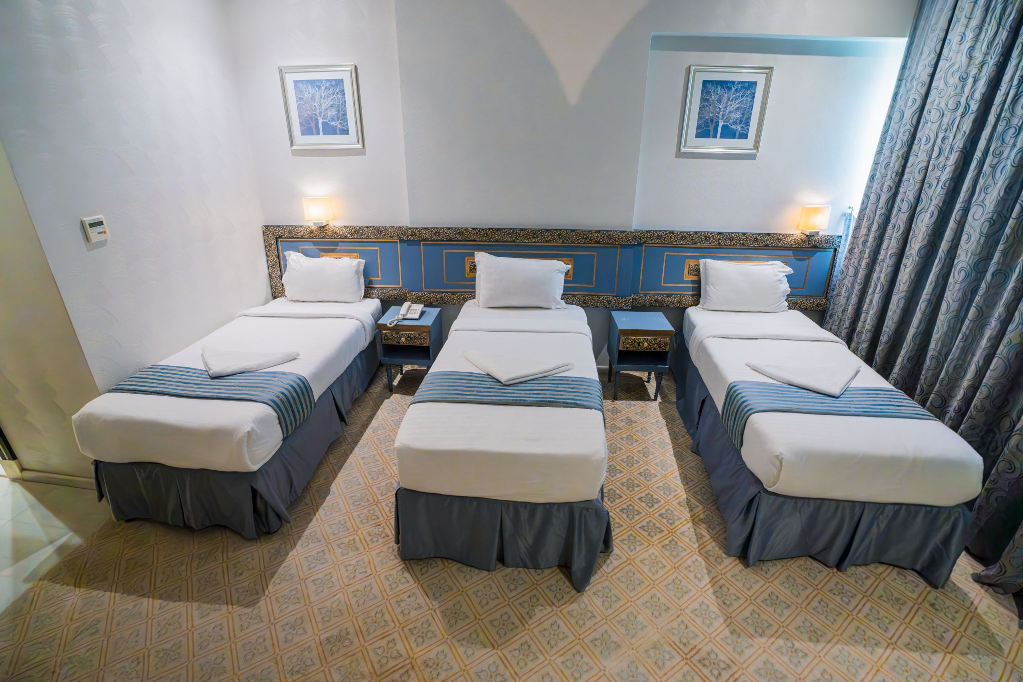 Habitación de hotel con tres camas individuales, piso estampado y dos cuadros en la pared.