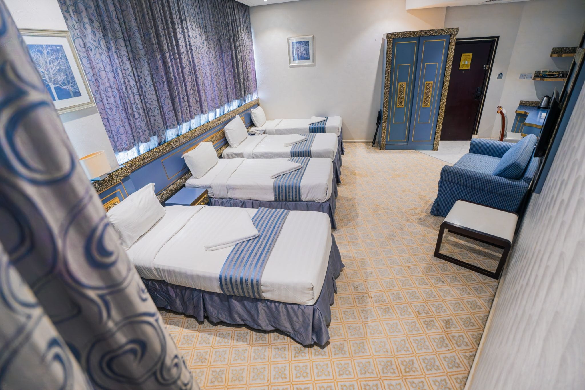Quarto de hotel com quatro camas de solteiro, um sofá, uma mesinha e um guarda-roupa.
