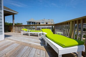 A wooden deck with two white lounge chairs with green cushions, a covered area, and a house in the background. - Private Semi-Oceanfront Retreat with Pool & Spa (Corolla)