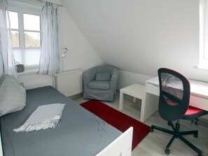 Ein Schlafzimmer mit Bett, Schreibtisch, Stuhl, Heizkörper und einem Fenster mit Vorhängen.