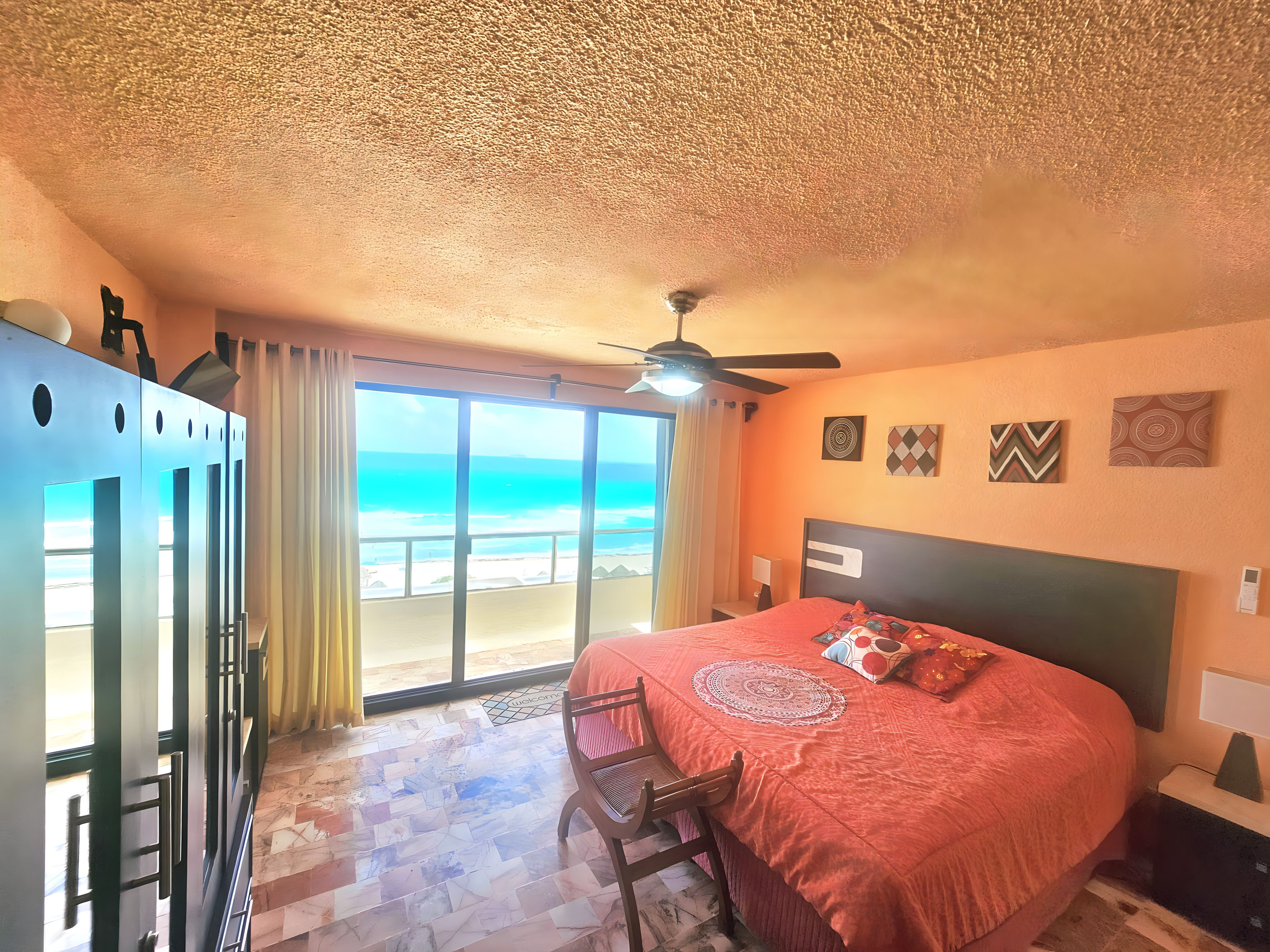 A bedroom with a bed, a ceiling fan, a view of the beach, and a door with a handle.