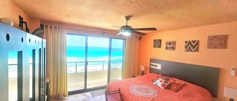 A bedroom with a bed, a ceiling fan, a view of the beach, and a door with a handle.