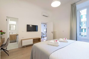 A hotel room with a bed, a TV, a desk with a chair, a bathroom, and a window with curtains. - Charming 1BR Apartment with Balcony near Vatican — Prati, Rome (Rome)