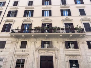 A multi-story building with a classical facade, featuring a central entrance with a dark door, multiple windows with shutters, and a balcony with plants. - Charming 1BR Apartment with Balcony near Vatican — Prati, Rome (Rome)