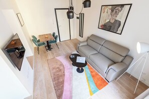 A modern living room with a grey sofa, a dining table with chairs, a coffee table with a laptop, and a colorful rug. - Charming 1BR Apartment with Balcony near Vatican — Prati, Rome (Rome)