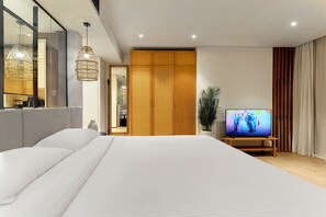 Ein modernes Hotelzimmer mit einem großen Bett, einem Fernseher auf einem Holzboden, einem Spiegel und einer Zimmerpflanze.